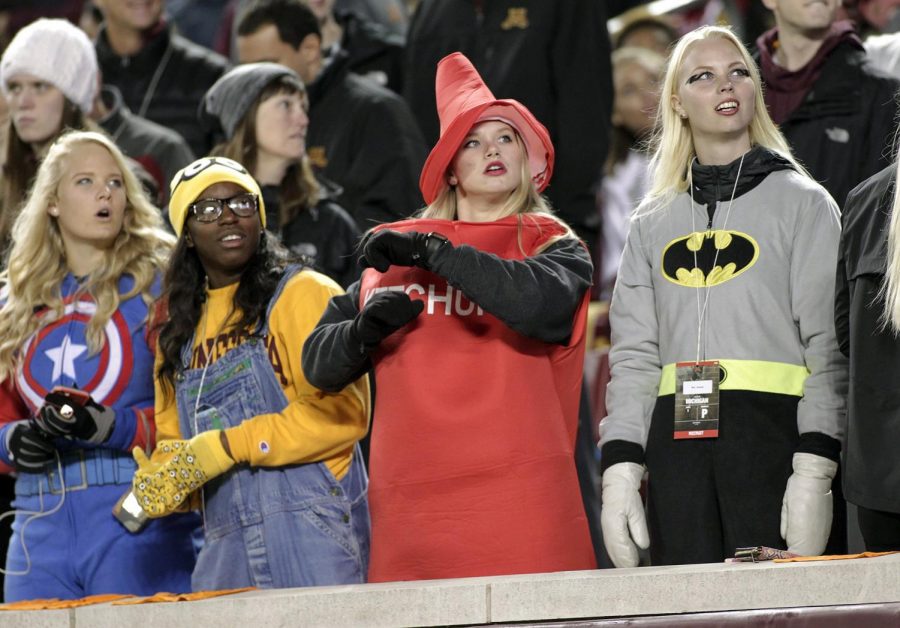 Four young girls dress up in respectful costumes for Halloween while they stand in the bleachers while watching a game. 