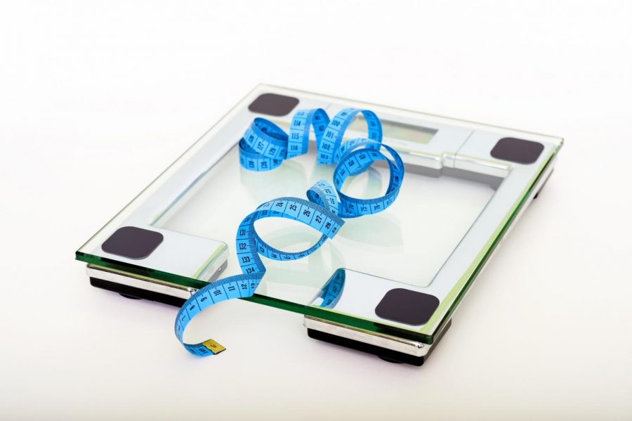A scale, usually used to measure body weight, sits next to a ruler. A scale is used to measure progress in weight gain or weight loss, but is not the only way to measure progress.