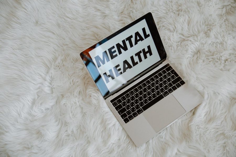 A laptop displaying the words Mental Health on the screen that is laid on a white faux carpet. 
