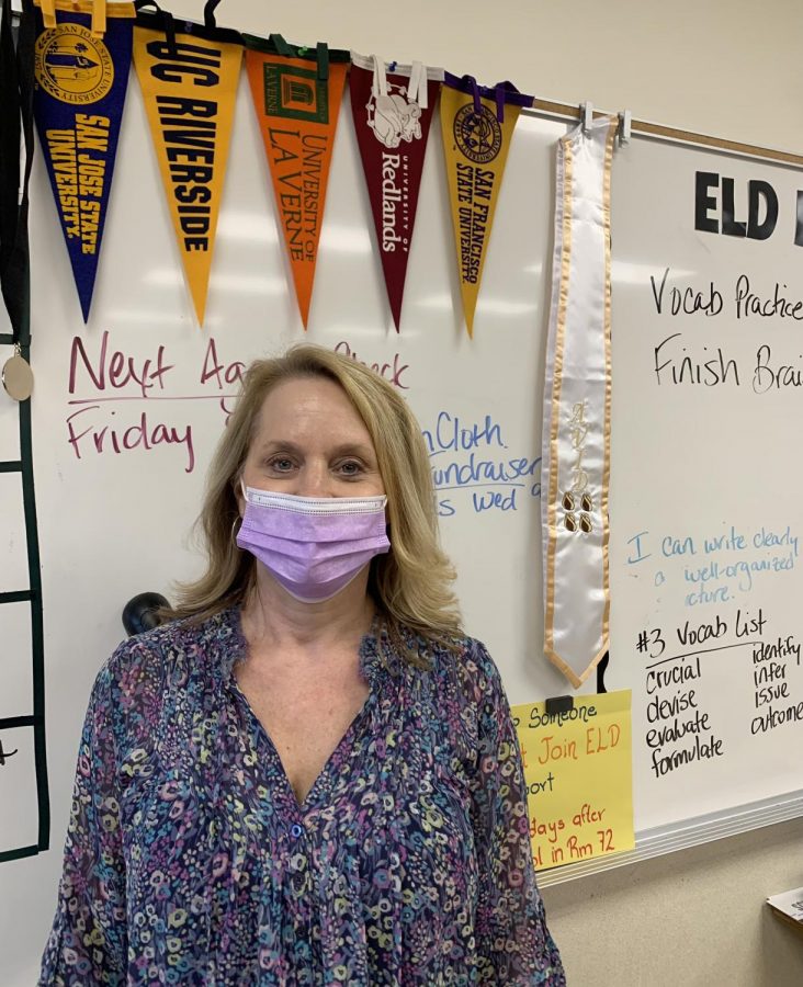 Mrs. Dominguez standing in front of the college banners present in her classroom. Avid teachers promote to Avid students going to a 4-year university. 