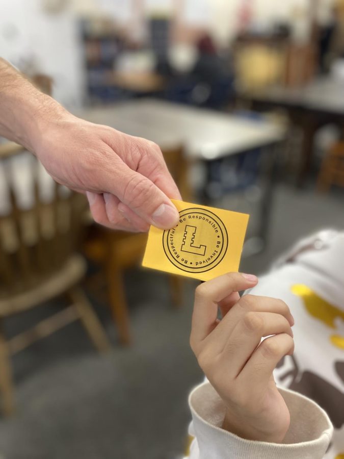 Close up picture of Mr. Crisafi handing a student a Lugo coin. 