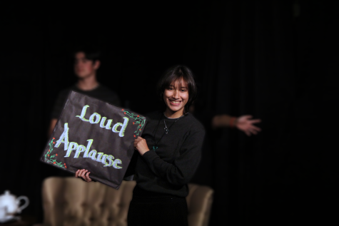 Emily Mendez holding the cue card telling the audience to cheer for the actors on stage. 